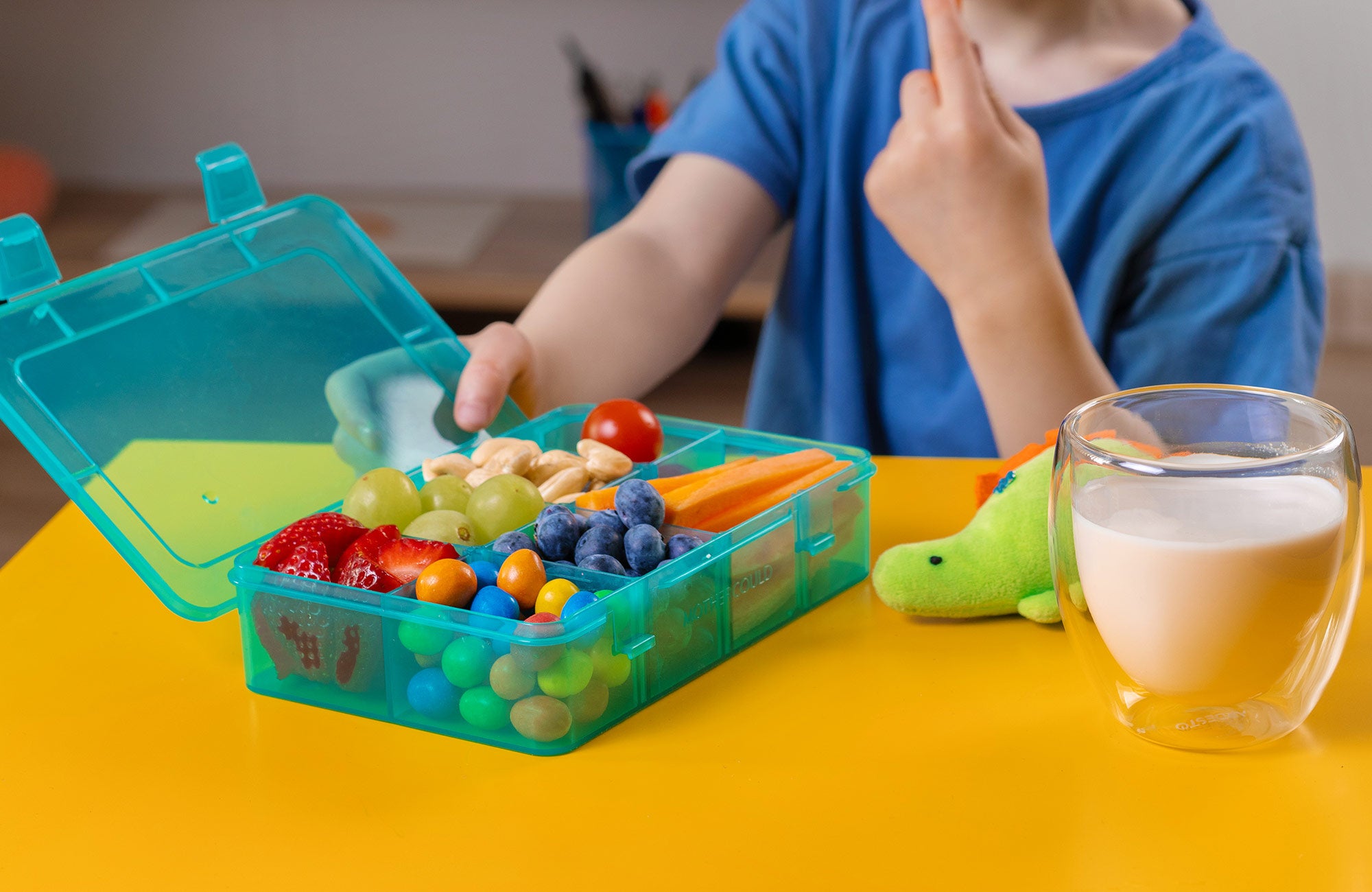 A child enjoying a variety of snacks from the Mothercould Snack Box Set, featuring 8 adjustable compartments.
